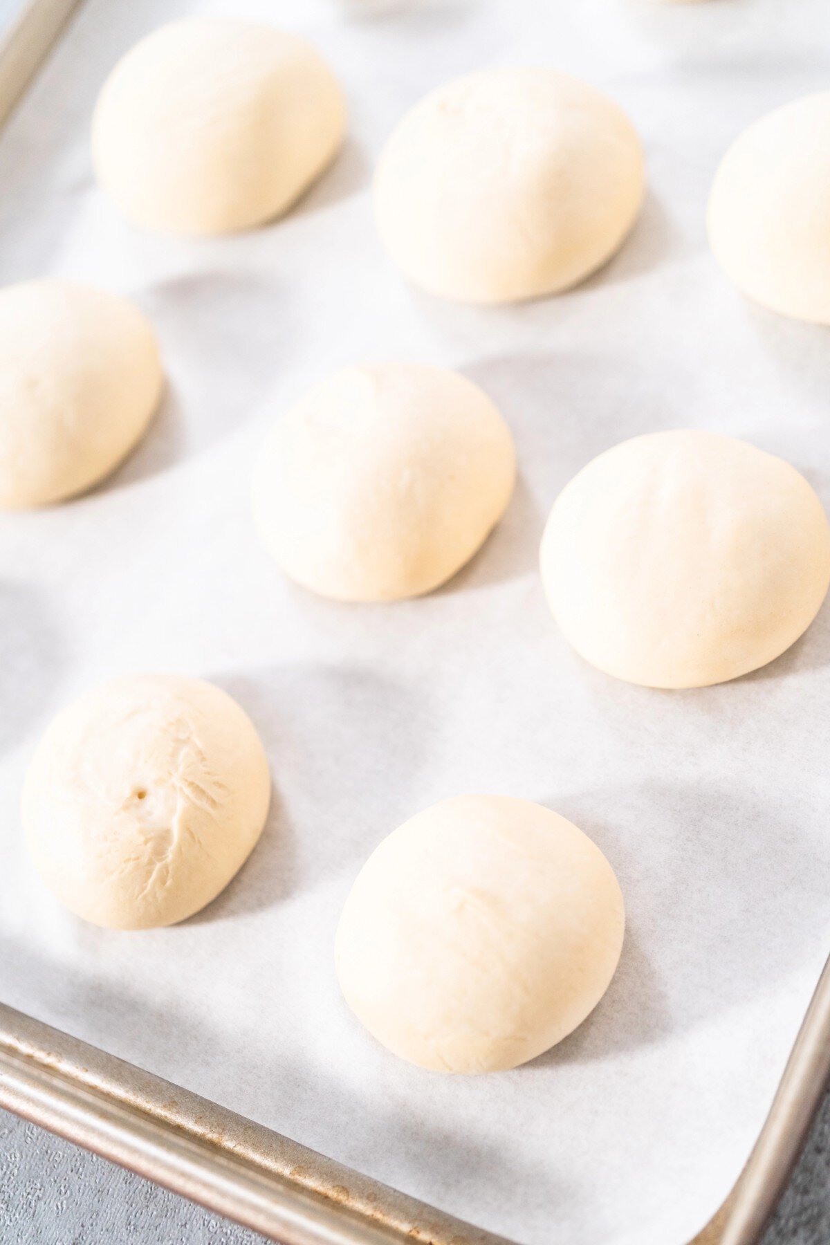 Rolls rising on a parchment lined baking sheet. 