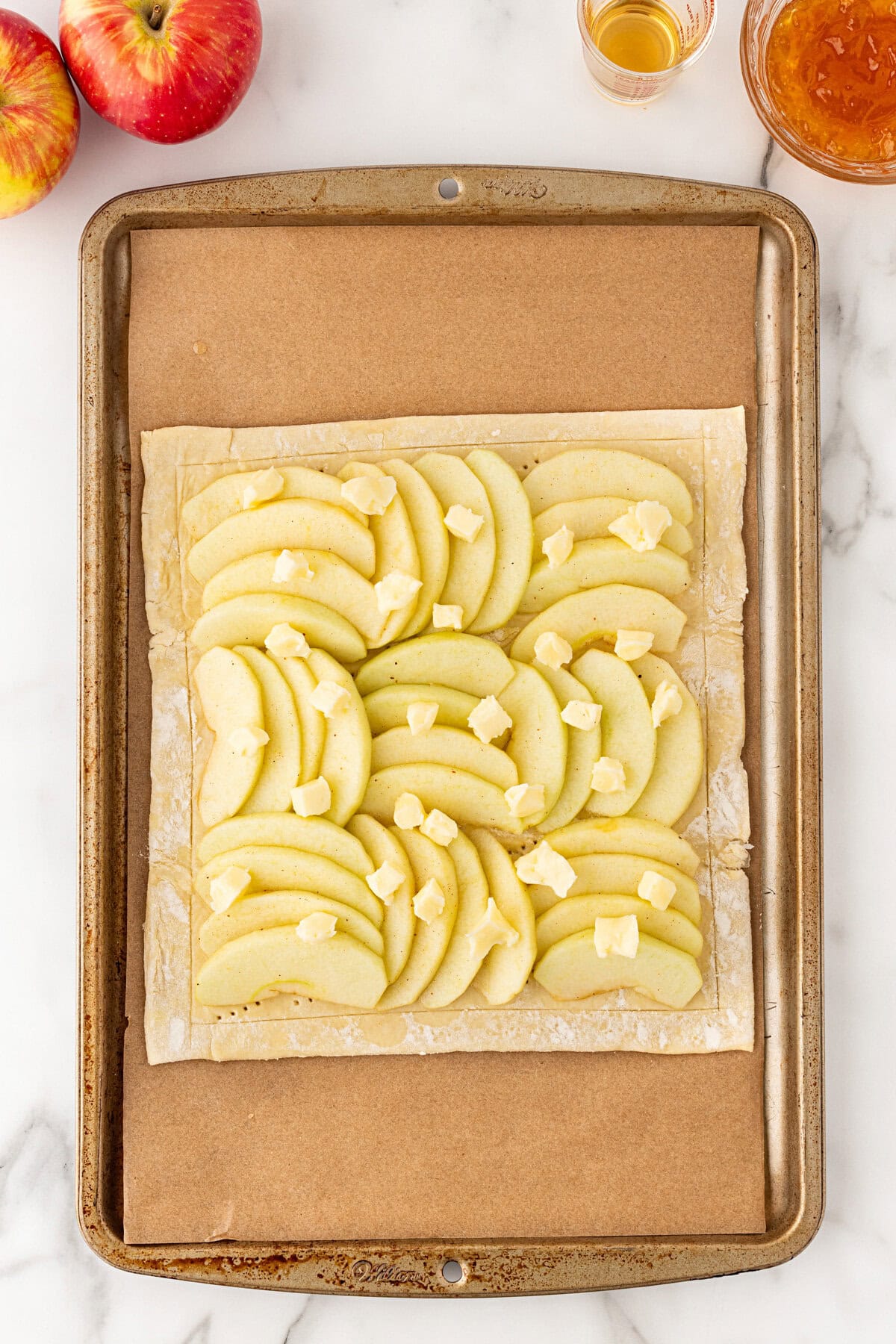 Laying the apple slices on the pastry and dollops of butter on top.