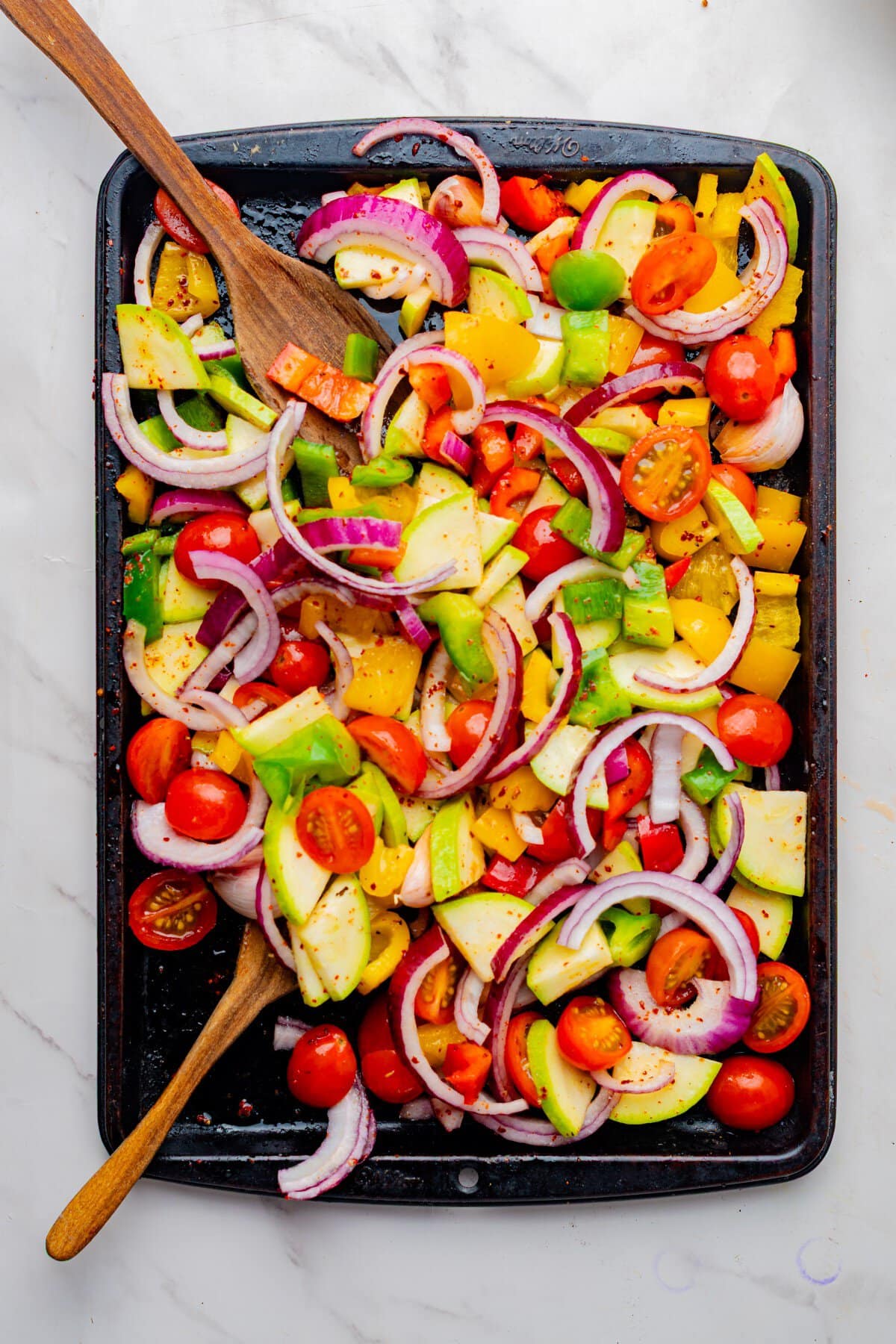 Seasoned veggies tossed on a baking sheet.