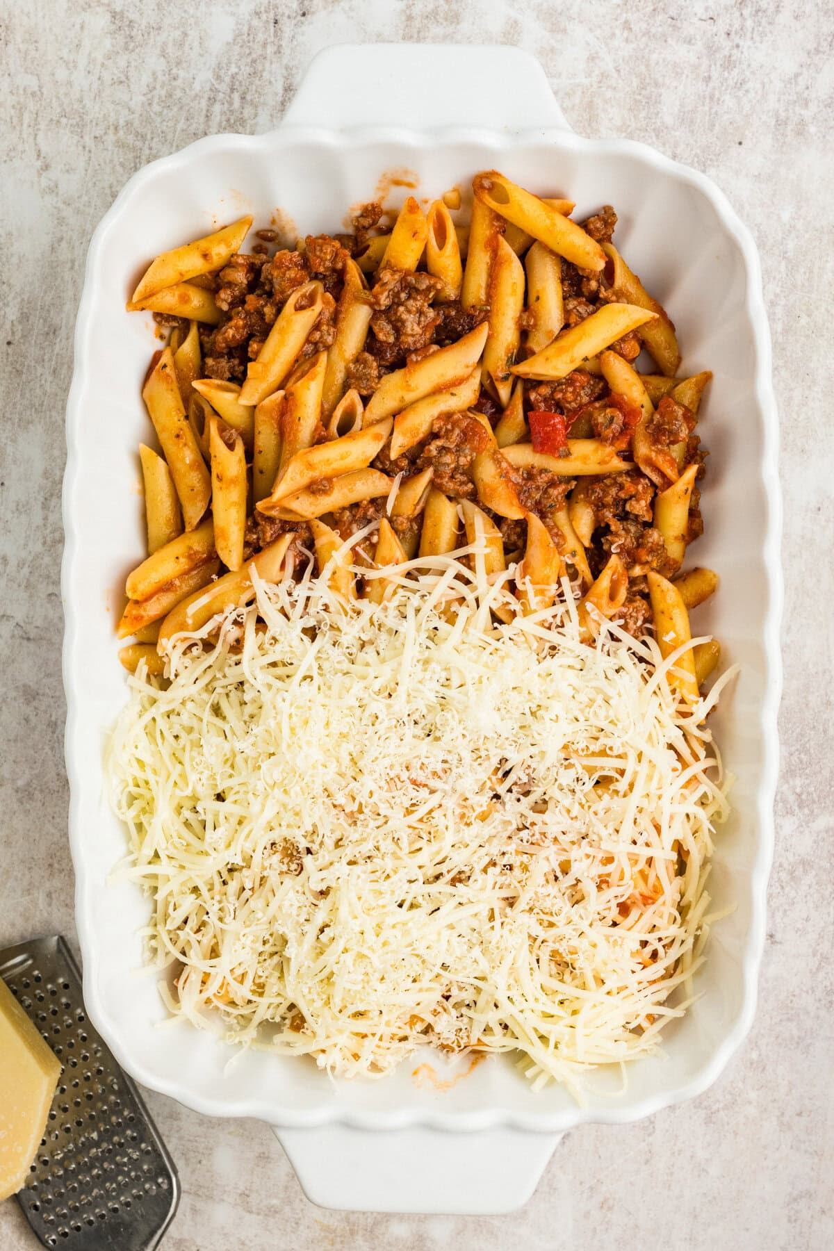 Layering the pasta mixture and cheese in the casserole dish.